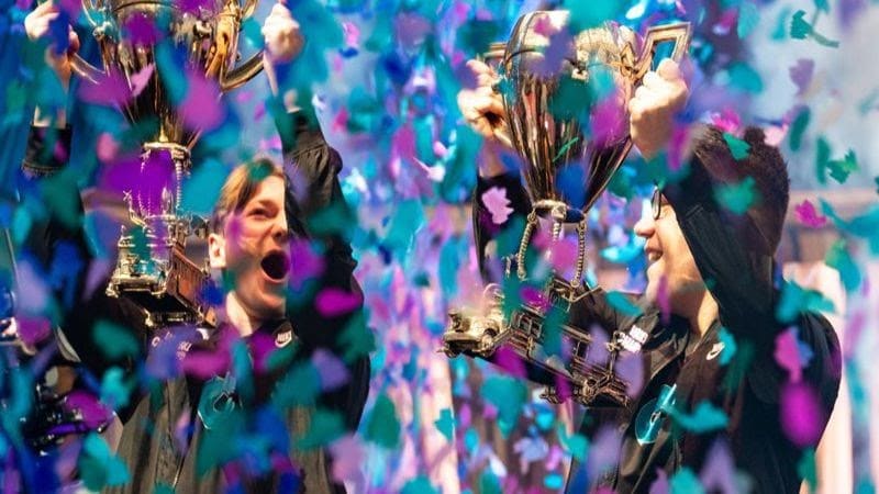 Aqua and Nyhrox grin and cheer at one another on stage as confetti falls on them after winning the Fortnite World Cup