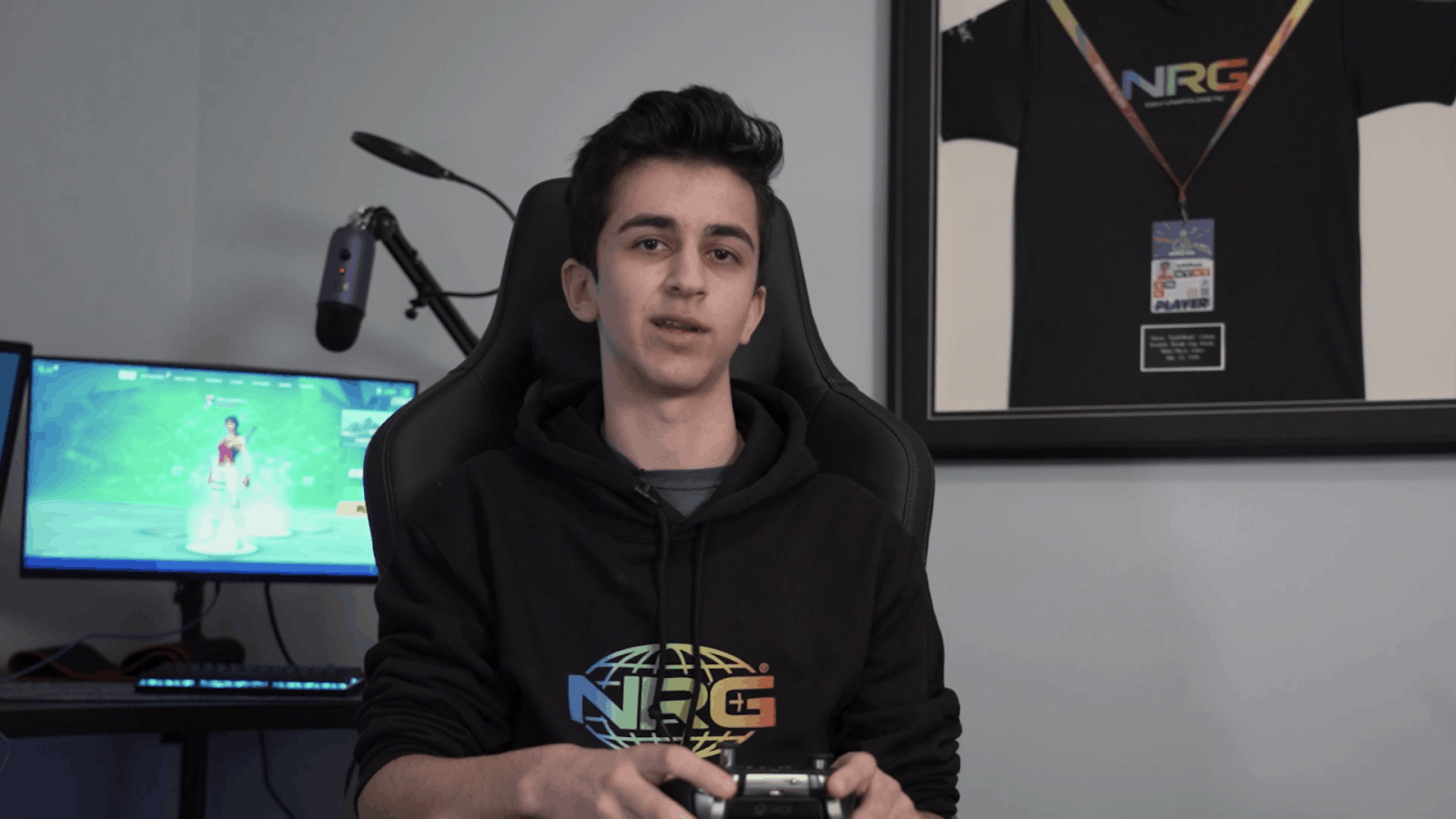 EpikWhale sits facing the camera in his gaming chair, holding his controller. He is wearing a black hoodie with the NRG logo.