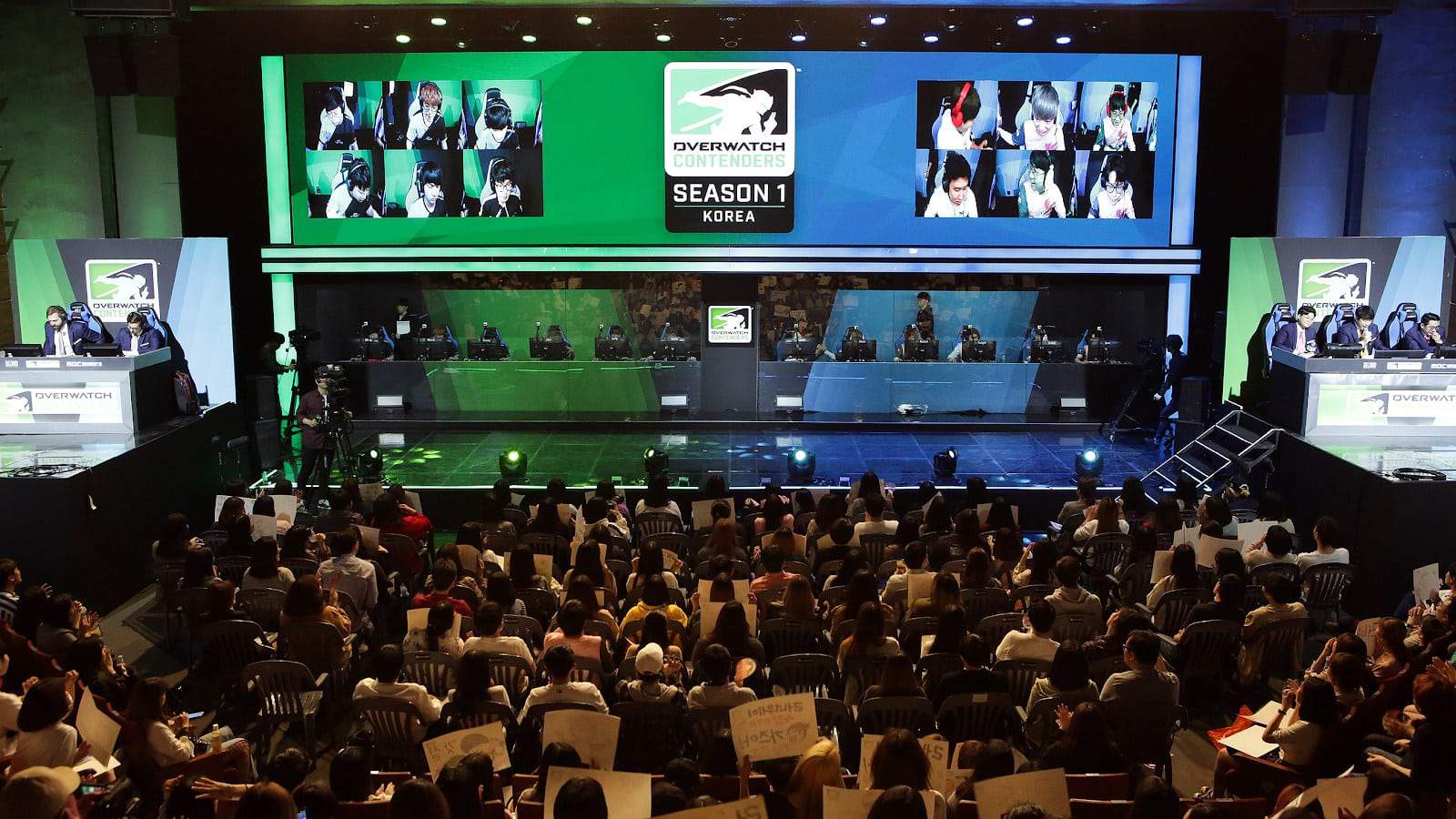 Korean fans sit with signs, cheering on players during a live series of Ovewatch Contenders