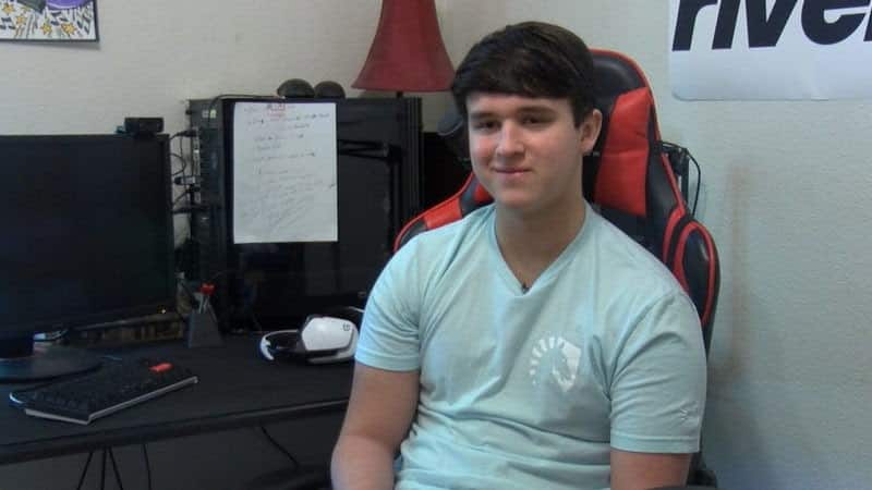 Pro Fortnite player Riversan sitting at a computer setup with a smirk