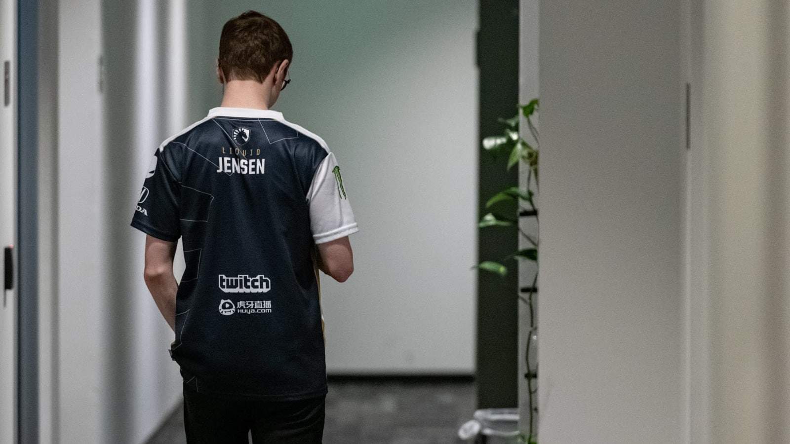 Team Liquid's mid laner Jensen walks down a hallway facing away from the camera