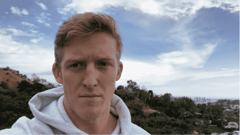 Turner "Tfue" Tenney stands against a blue sky with a serious expression as he looks at the camera