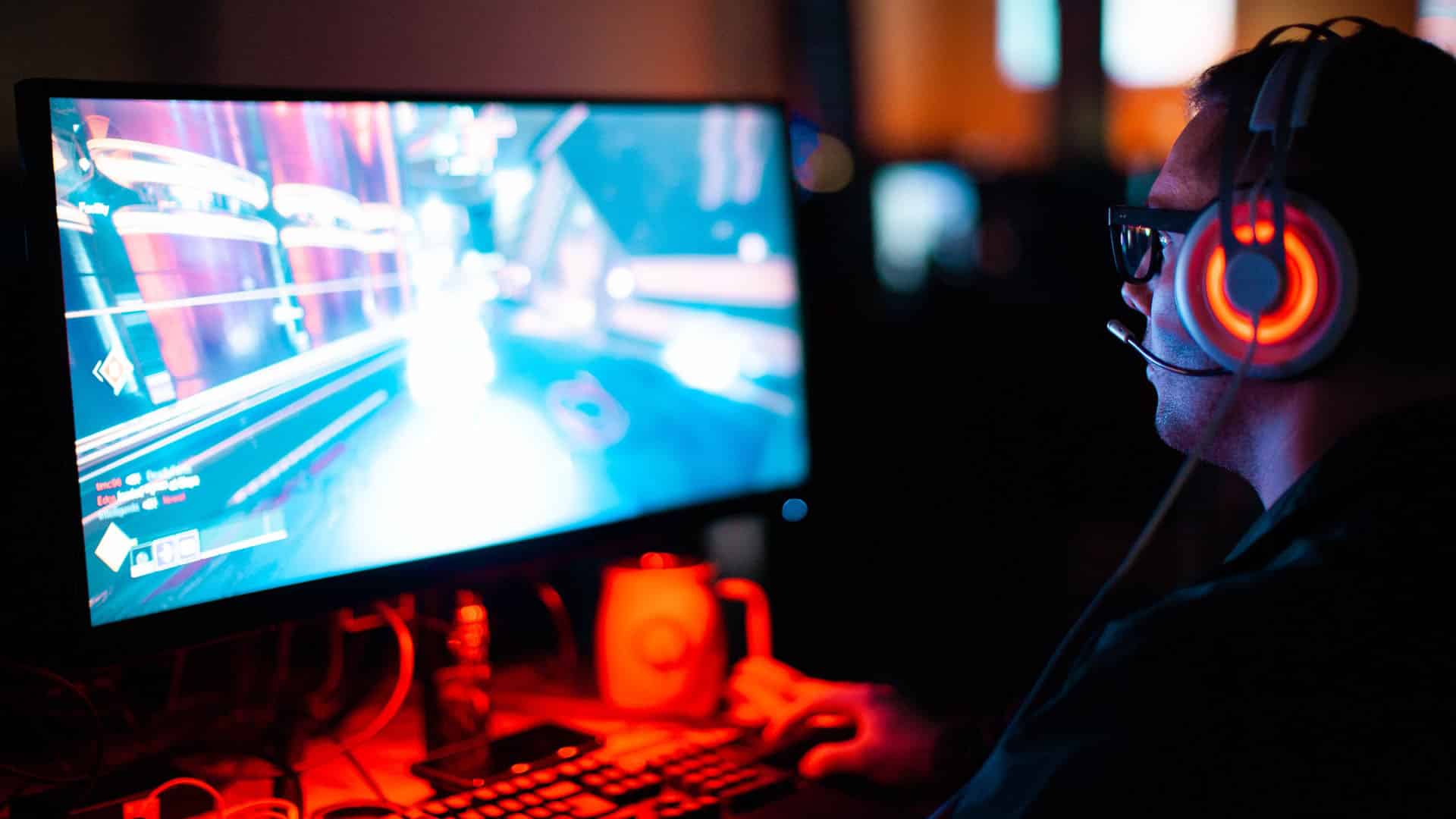 A gamer wearing a red and black headset sits at their PC playing