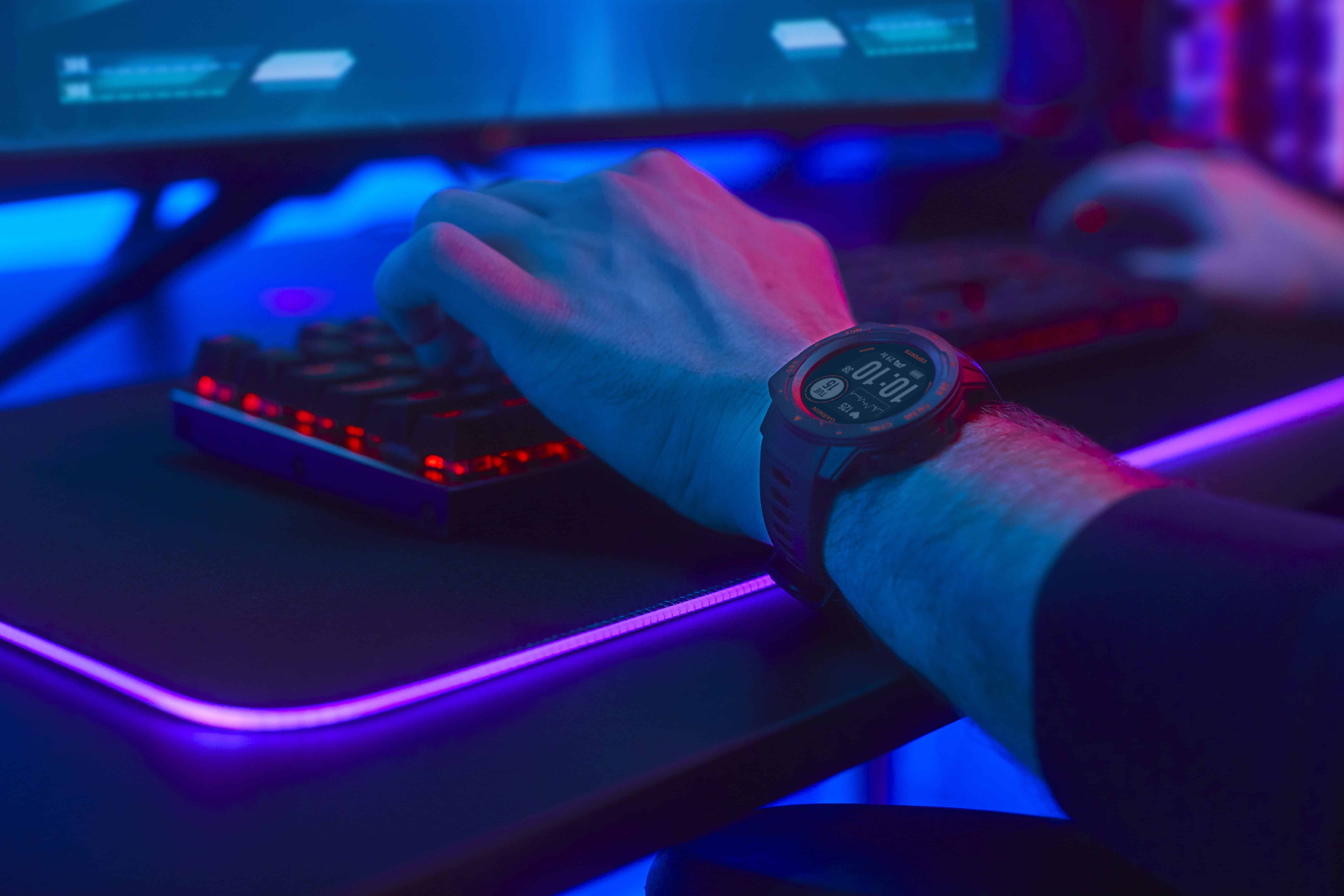 A gamer playing at a computer with a Garmin Instinct Esports Edition smartwatch on