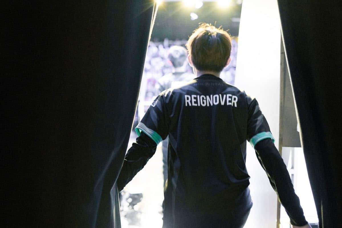 LoL former player and current C9 coach Kim "Reignover" Yeu-jin steps out into a stage's spotlight from behind curtains wearing a jersey with his name on it