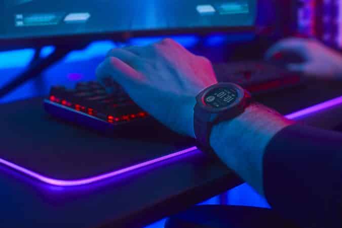 A gamer playing at a computer with a Garmin Instinct Esports Edition smartwatch on