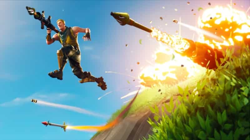 A male Fortnite character jumps over a hill with an RPG and a bunch of rockets shooting from behind him