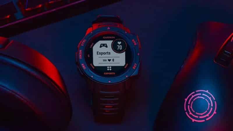 The Garmin Instinct Esports Edition smartwatch lies in between two gaming mouses lit up by a computer monitor
