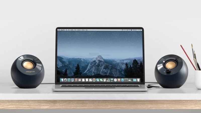 A laptop is shown open at an office work station with the Creative Pebble V3 speakers flanking it