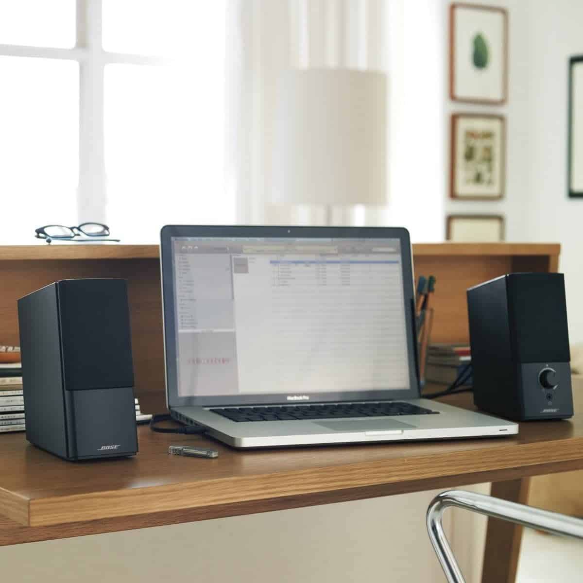 A laptop is shown open at an office station with the Bose Companion 2 Series III speakers on the sides