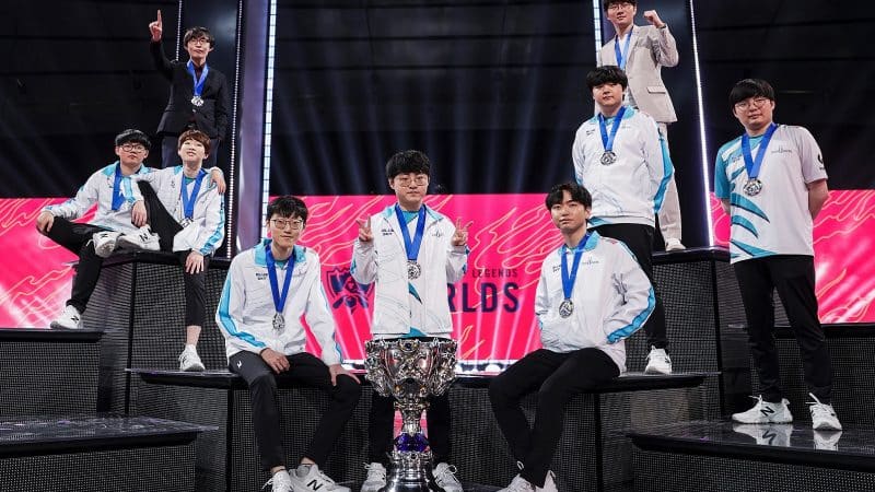 The Damwon Gaming LoL roster poses across a stage with the Summoner's Cup front and center after their ultimate victory at the 2020 World Championship