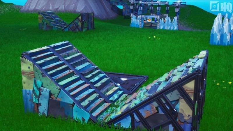 Two wooden, colorful half-staircases are shown from Fortnite in a grassy field terrain with some other buildings and constructs in the background