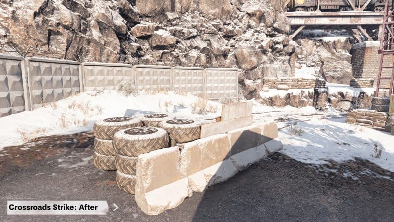 A screenshot from Call of Duty Black Ops Cold War map Crossroads post-map changes. A cement roadblock with tires behind it is in the corner of the map with a wall and rock face behind them