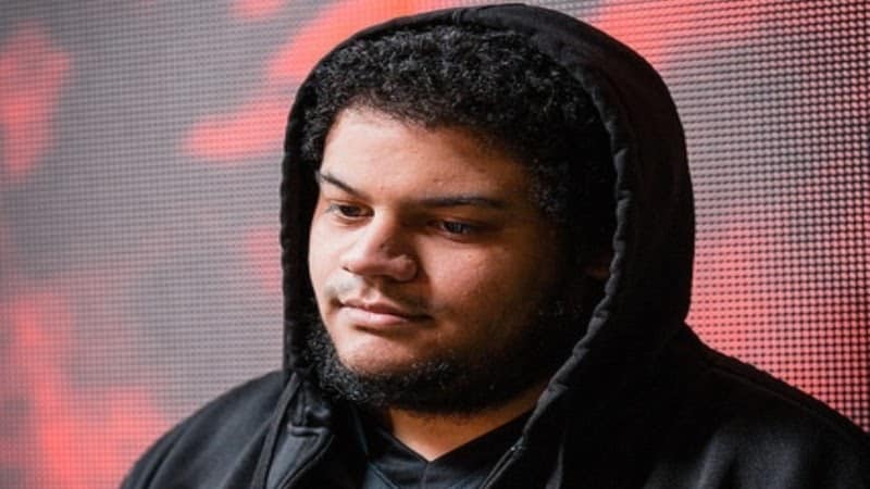 Pro Dota 2 player Andrew "Jubei" Evelyn wears a hoodie with a screen behind him and looks downwards.