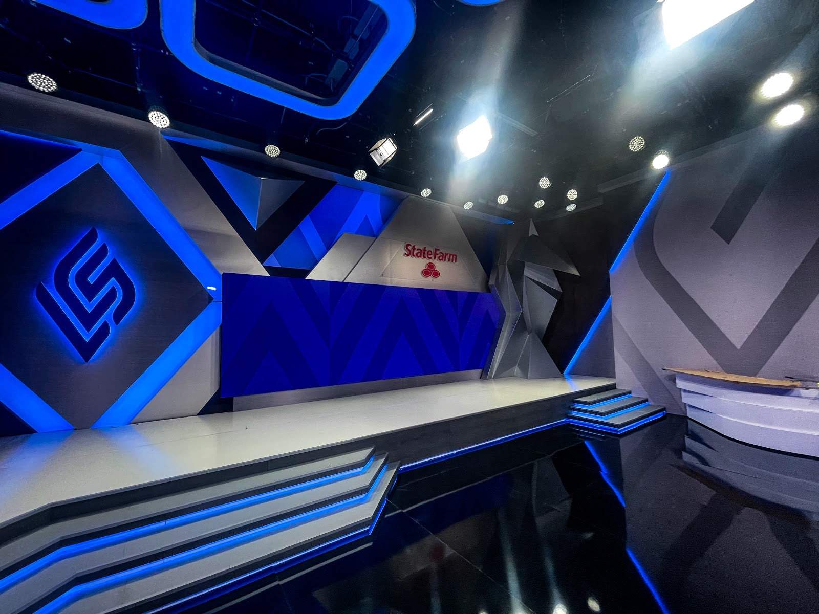 The LCS studio in Los Angeles, California with the LCS logo on one of the walls, with sharp blue and gray designs . A State Farm logo is on a monitor as well.