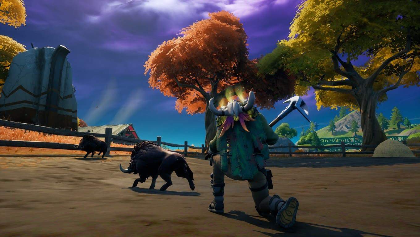 A player character kneels on the ground, stalking two boars in the game Forntite. The tops of farm buildings crest over a hill with a purple sky above.