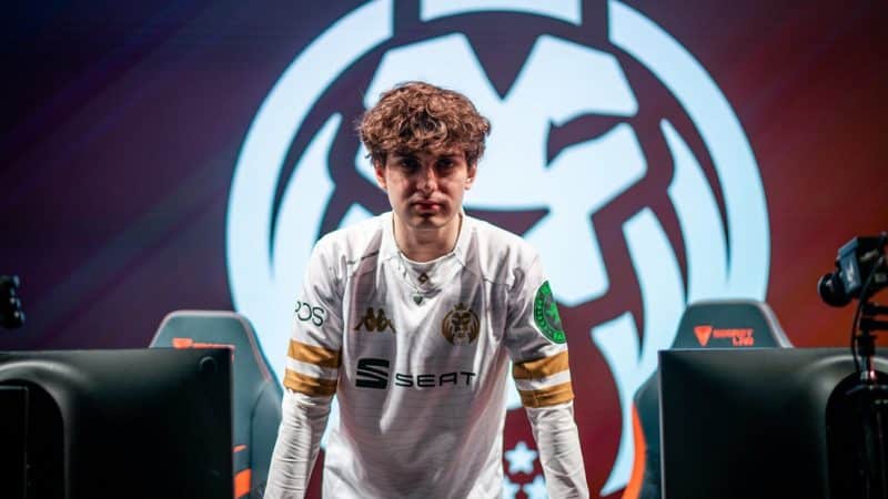 Pro LoL ADC player for MAD Lions Carrzy leans forward on a desk with the MAD Lions lion head logo behind him.