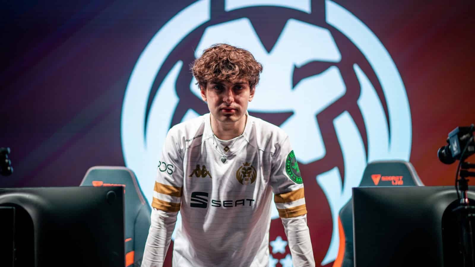 Pro LoL ADC player for MAD Lions Carrzy leans forward on a desk with the MAD Lions lion head logo behind him.