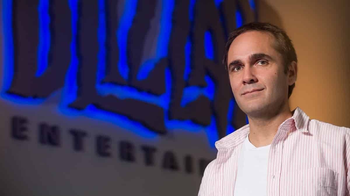 Aaron Keller smiles next to a large, wall mounted Blizzard logo.