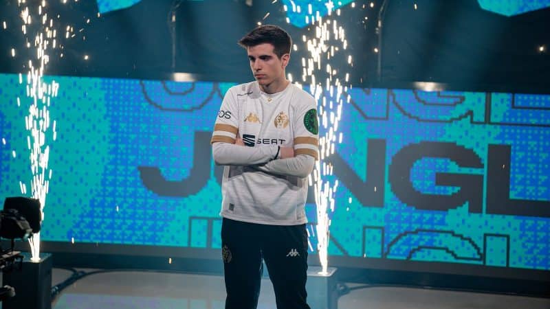 MAD Lions' Javier “Elyoya” Prades Batalla crosses his arms in front of a camera with sparks flying behind him.