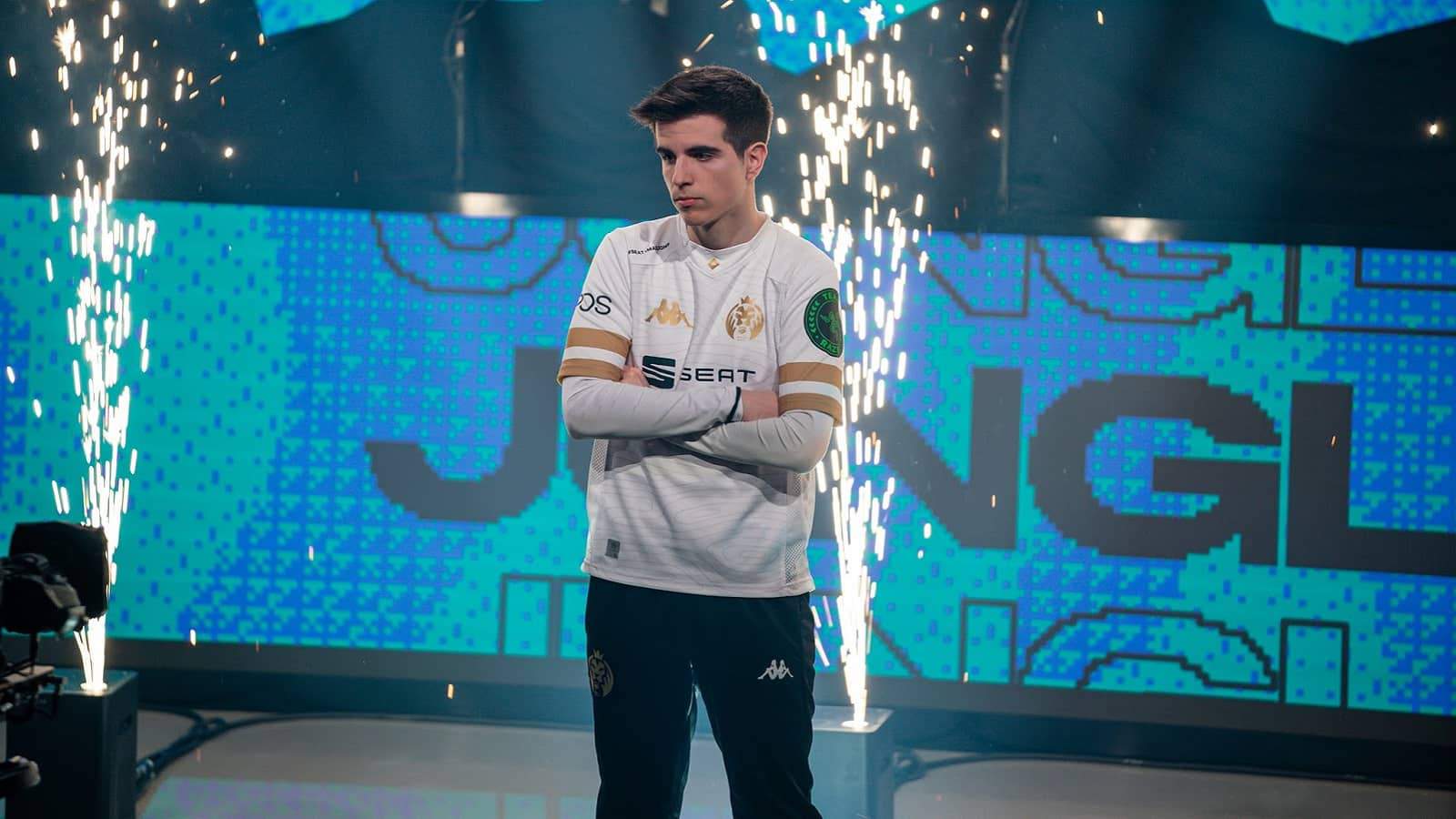 MAD Lions' Javier “Elyoya” Prades Batalla crosses his arms in front of a camera with sparks flying behind him.