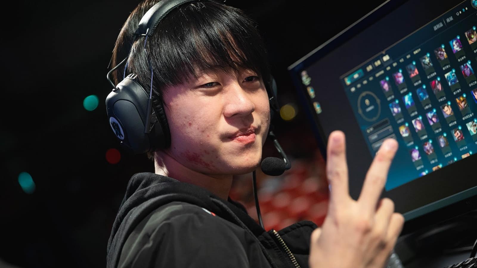 RNG Shi “Ming” Sen-Ming holds up a V sign with his hand in front of a PC with LoL on it.