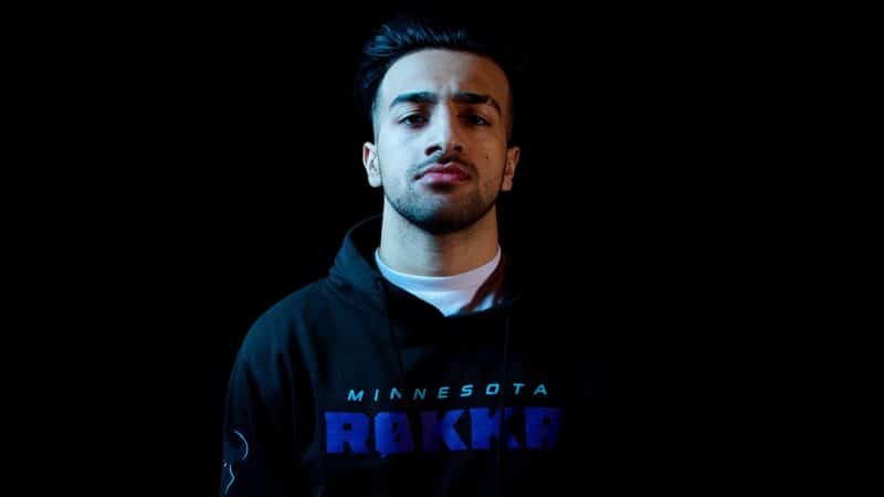 Obaid "Asim" Asim stands against a black background under low lighting wearing his Minnesota Rokkr hoodie