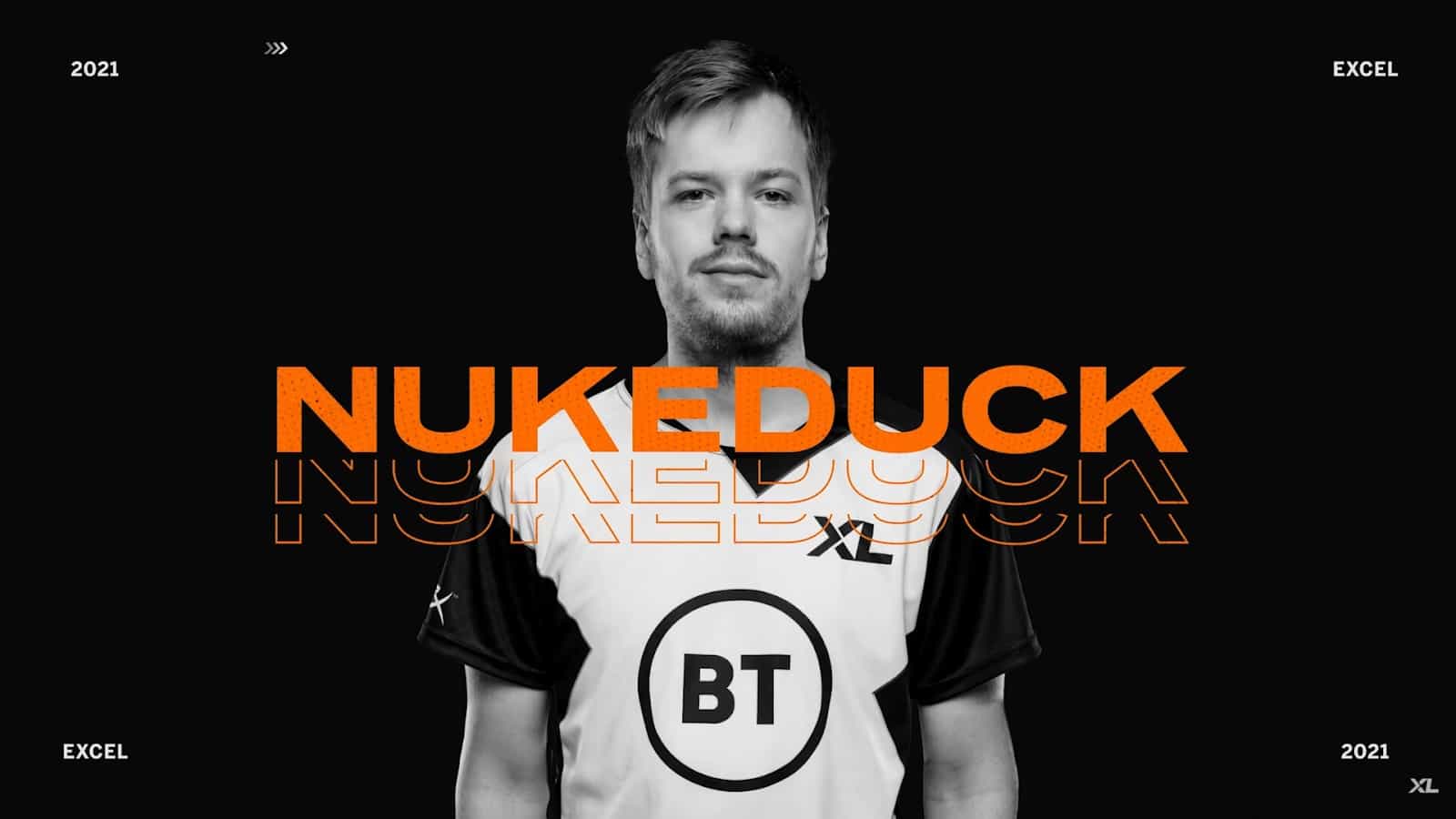 Pro LoL player Erlend "nukeduck" Våtevik stands with an Excel Esports jersey on and his gamertag in orange in front of him.