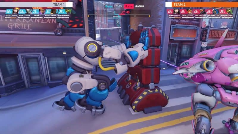 An in-game screenshot of Overwatch 2's Push mode, focusing on robot T.W.O. pushing a large barrier.