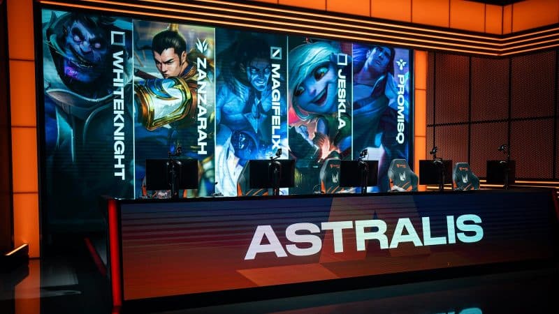 The LEC stage is lit up in orange lights with two large monitors, the larger on showing the LoL champions Dr.Mundo, Xin Zhao, Sylas, Tristana and Taric and the other with the team name Astralis.