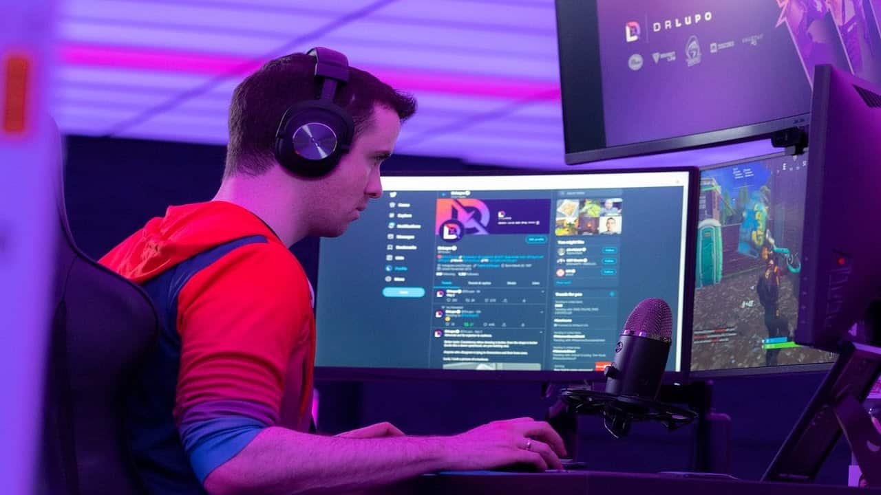 Video game streamer and content creator Benjamin “DrLupo” Lupo plays Fortnite at his PC in a dimly purple lit room.