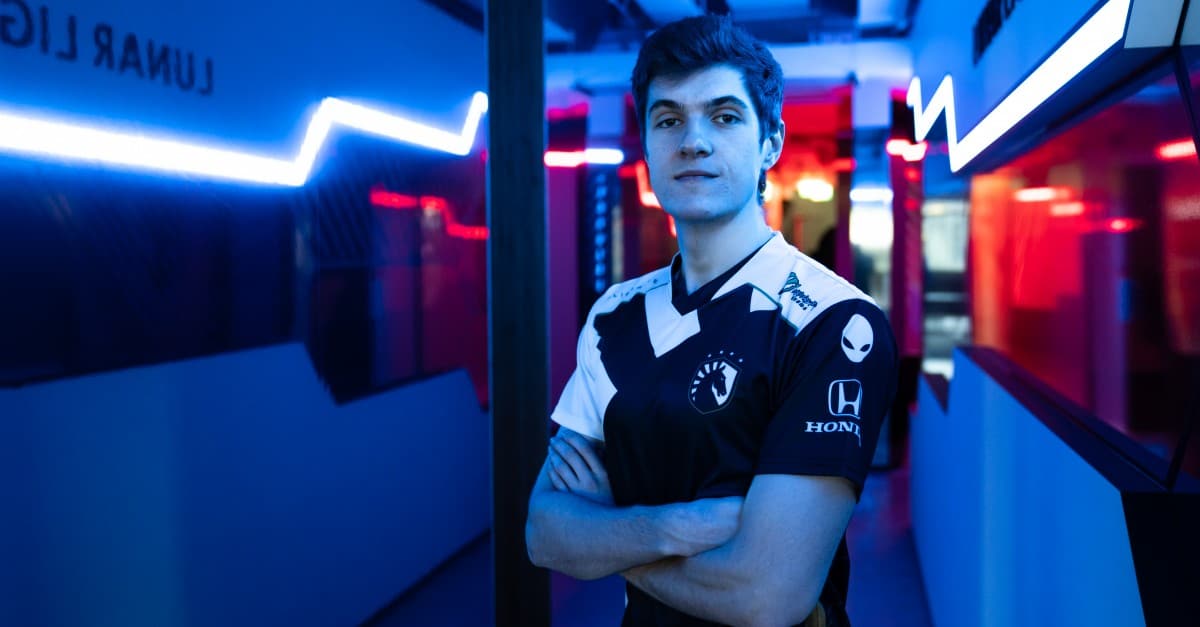 Barney "Alphari" Morris stands with his arms folded wearing a Team Liquid jersey in a dark hallway lit up with varied colored lights.