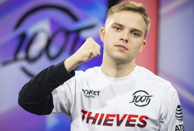 Pro LoL player for 100 Thieves Felix "Abbedagge" Braun puts his fist in the air with a 100T logo behind him.