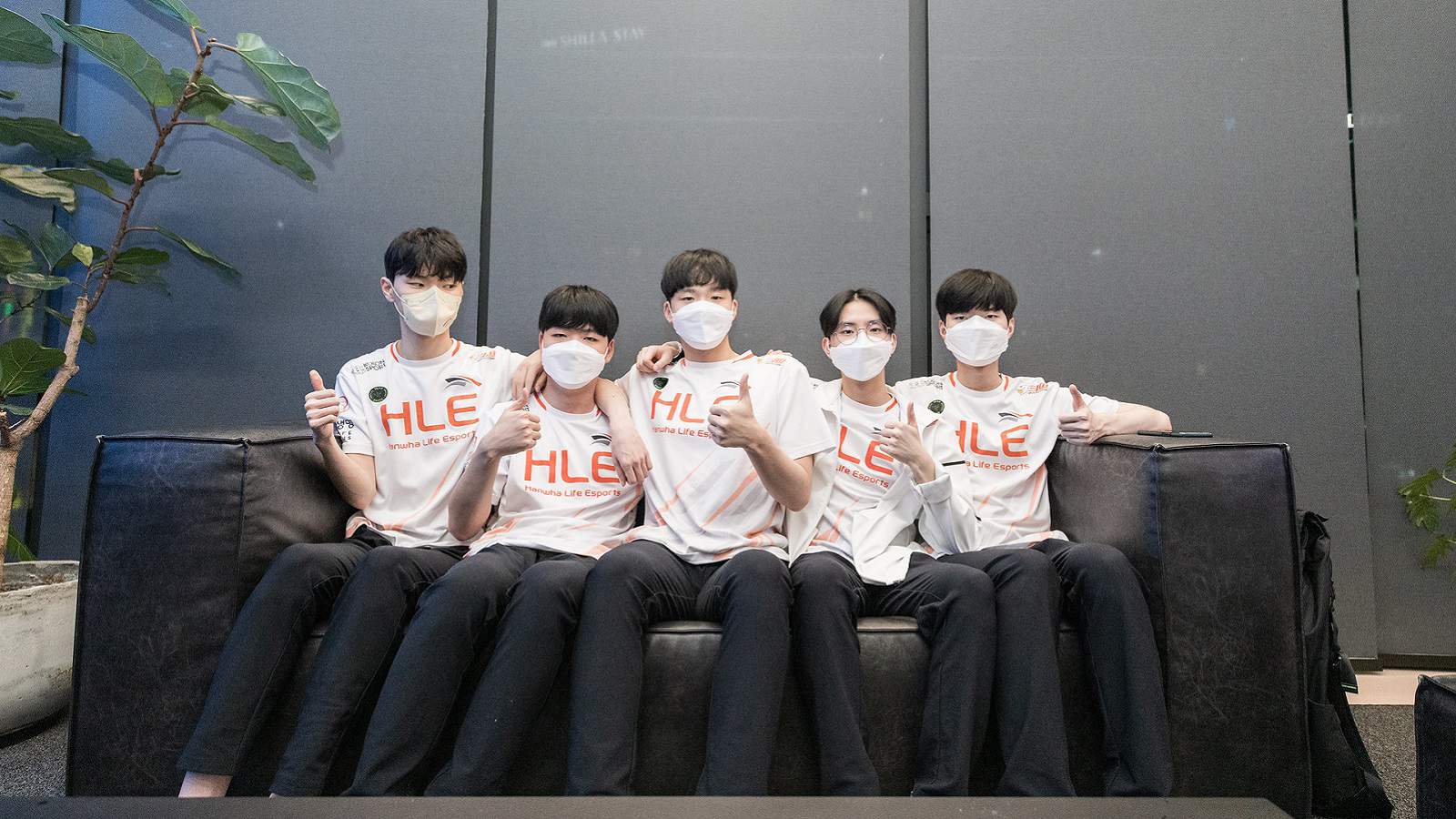 The Hanwha Life Esports LoL team sits together on a couch and gives the camera thumbs up.