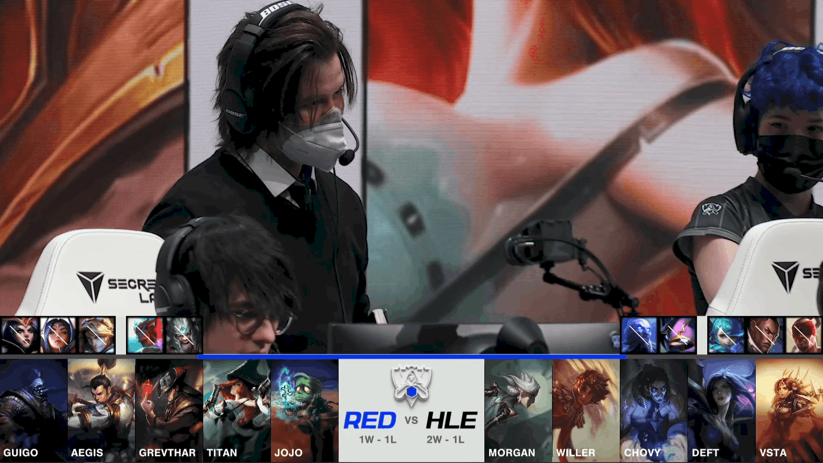A screenshot from the 2021 World Championship Play-ins broadcast, showing the drafts between RED Canids and Hanwha Life Esports with a shot of coach Coelho on stage in the middle.