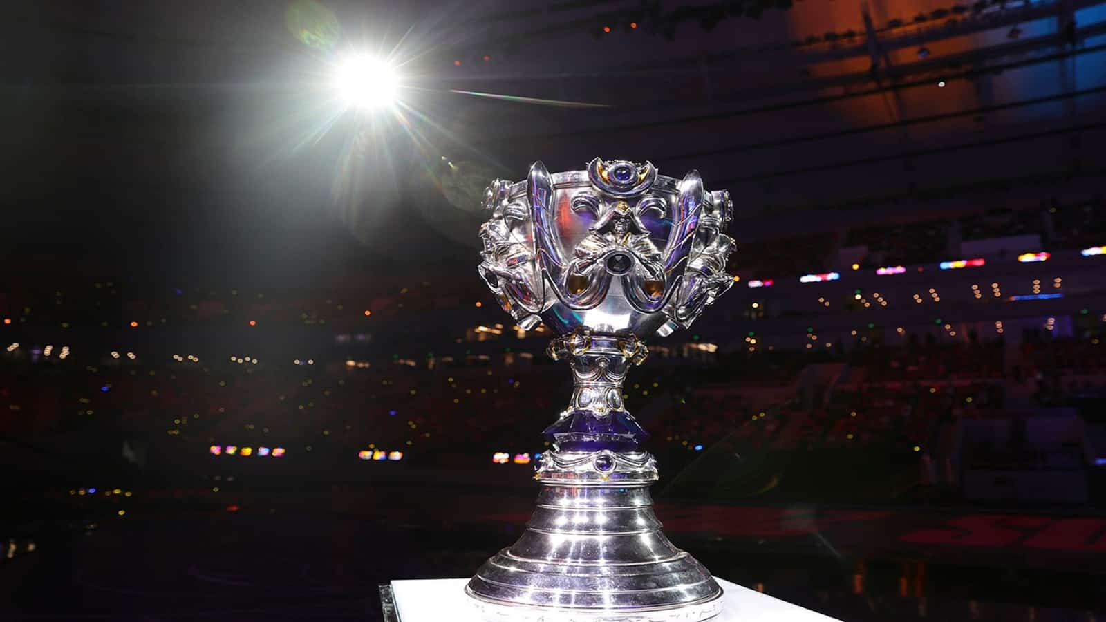 The Summoner's Cup from the LoL World Championship stands tall on a podium with a spotlight illuminating it.