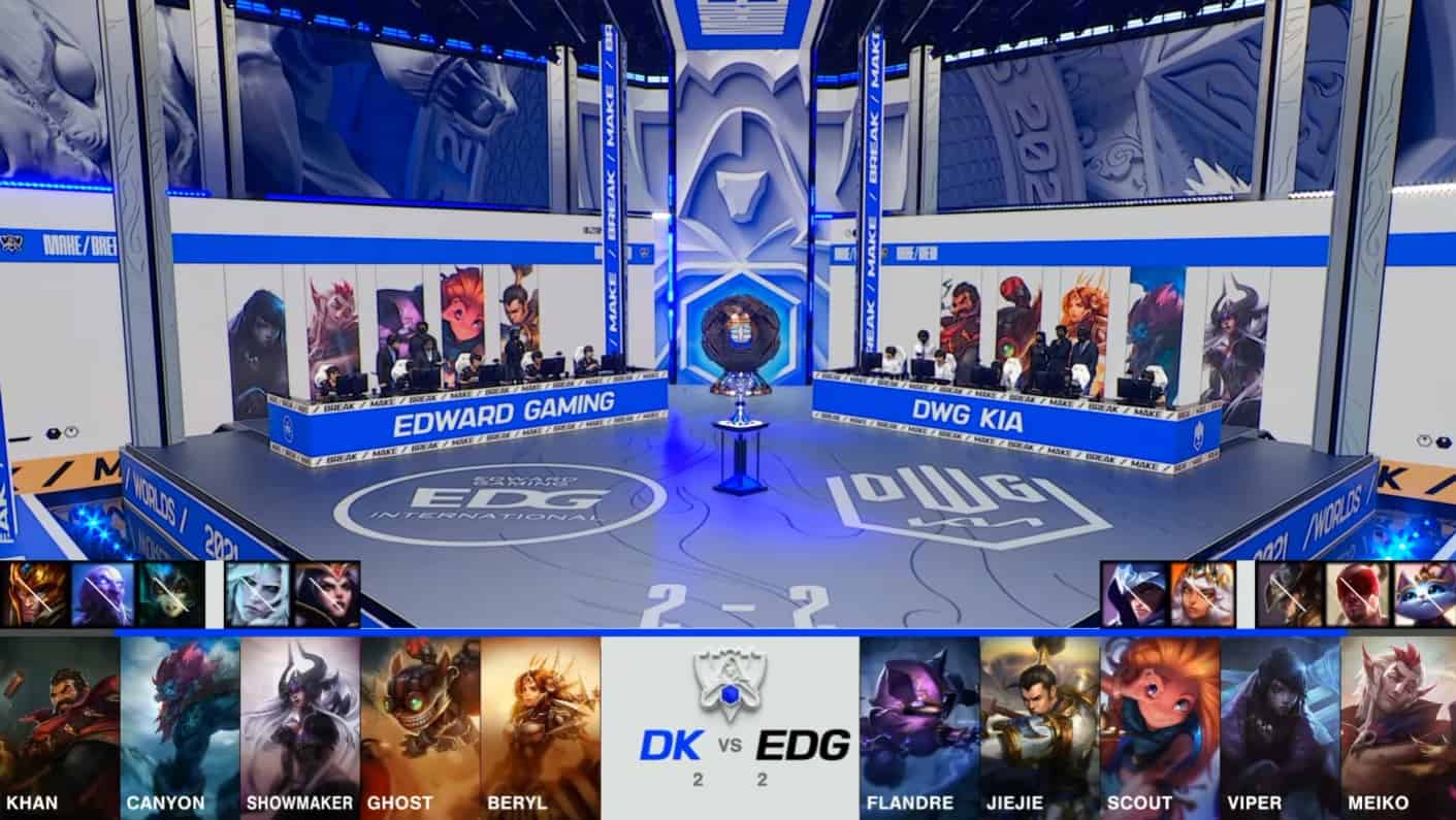 A screenshot from the 2021 LoL World Championship Grand Finals broadcast, showing the Game Five champion drafts between DAMWON KIA and Edward Gaming with a shot of both teams and the Summoner's Cup on the Worlds 2021 stage above.