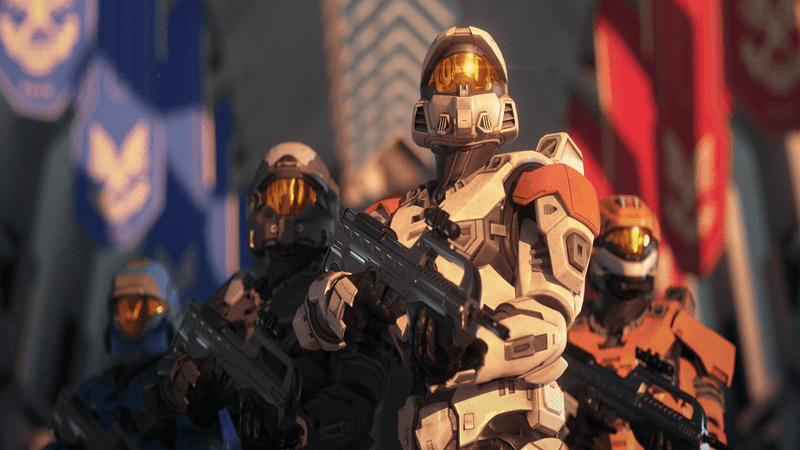 Four Spartans from Halo hold their weapons and look towards the sky with red and blue banners behind them.